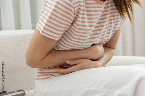 Картината върху платно Woman stomach pain abdomen ache cramp sitting sofa home discomfort, woman holdin