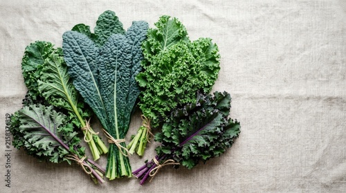 A collection of fresh kale leaves rests on a textured linen cloth. The kale displays a variety of colors, including dark green, lighter green, and purple hues.