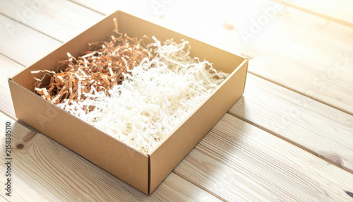 Open Cardboard Box Filled With White and Brown Shredded Paper On A Light Wooden Surface