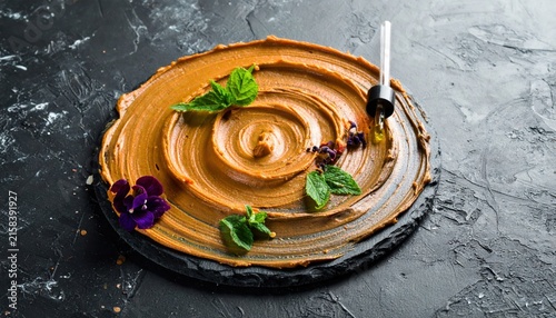 Swirling creamy peanut butter dessert expertly garnished with fresh mint and edible flowers on a dark slate plate