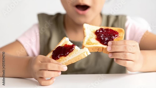 Child's hands holding and breaking toasted bread with sweet strawberry jam