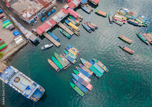Panoramic aerial perspective of Bitung port in North Sulawesi. The lively harbor teems with passenger boats and ferries, seamlessly blending the urban coastal landscape with lush distant mountains.
