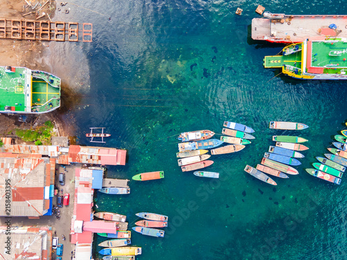 Top-down aerial view of colorful wooden passenger boats docked at Bitung port, Indonesia. These traditional vessels wait to ferry locals across the strait to Lembeh Island.