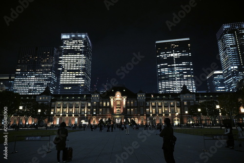 Fotografie 夜のライトアップに照らされた歴史的建築である東京駅丸の内駅舎と、その背後にそびえ立つ近代的な超高層ビル群の対比。都会的で洗練された秋の夜景。
