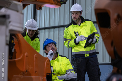 Industrial worker hard hat safety vest factory machinery engineer team inspection of equipment inside manufacturing plant with focused expression