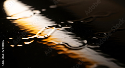 Abstract light reflection on dark liquid surface with glowing warm illumination and liquid ripples creating modern artistic background pattern