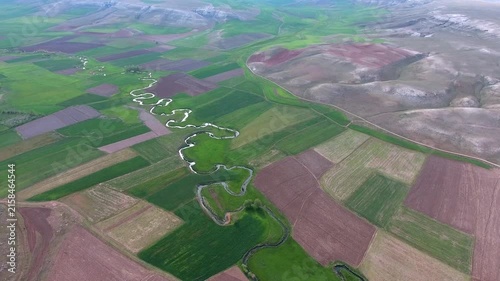 Meandering river winds through patchwork farmland, shaping green and brown floodplain fields.