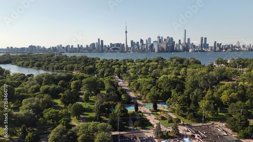 Aerial view tracking right over the lush green gardens, paths, and fountains of Toronto Islands with the iconic downtown city skyline and CN Tower beyond