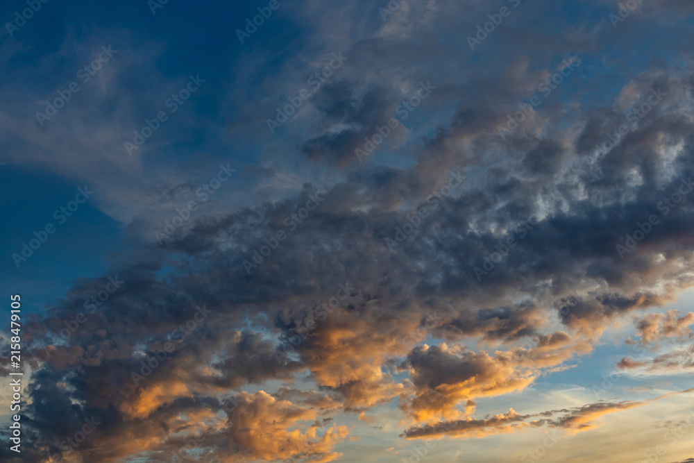Obraz premium Dramatic sunset cloud formations illuminated by golden orange light against a deep blue sky