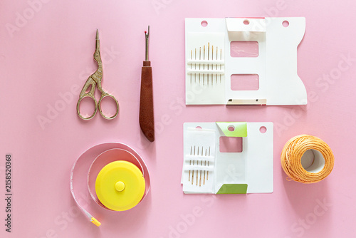 Sewing kit with scissors, seam ripper and thread spool on pink background