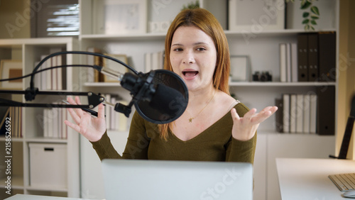Fotografía Young female podcaster speaking into a microphone while recording at home