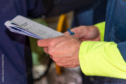 Close-up of a worker's hands holding a document, with workwear sleeves visible, representing professional work, documentation and routine activities in an industrial or maritime environment.
