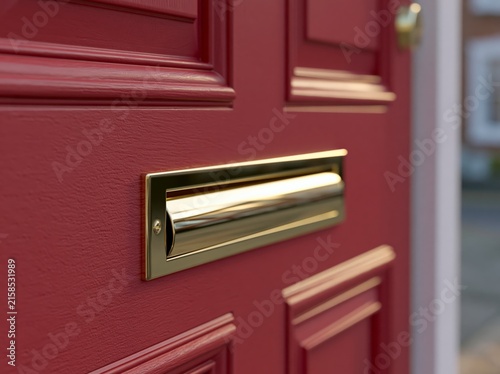 A close-up view of a red, panelled front door with a gleaming brass letterbox, highlighting classic home architecture and entry detail.