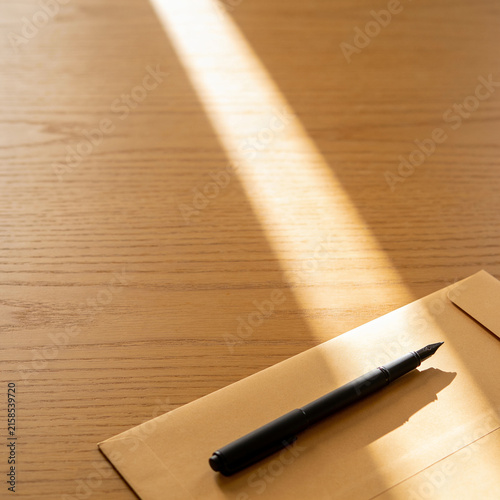 Black fountain pen on a craft envelope on wooden desk illuminated by natural beam of sunlight
