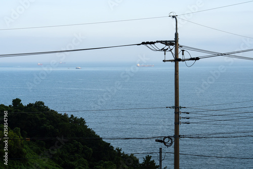 Tall Electrical Utility Pole Overlooking Vast Calm Sea and Distant Ships