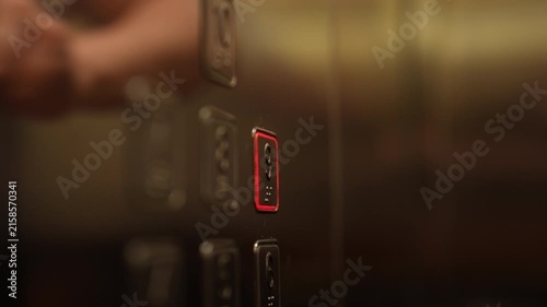 Female hand with fresh French manicure pressing illuminated call button on modern elevator panel, with reflection visible on shiny metallic surface, close-up, slow motion.