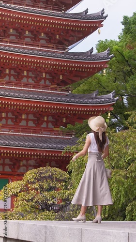 Vertical slow motion of an Asian woman visiting a traditional Japanese temple. She pauses by the red pagoda and looks around the sacred grounds.
