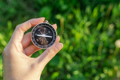 Bild auf Leinwand Hand holding a magnetic compass against a blurred green background, symbolizing navigation, direction, travel, adventure and finding the right path in nature