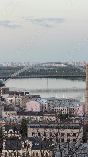 Kyiv cityscape at dusk with the Dnipro River, arched bridge, urban skyline and calm evening atmosphere. Panoramic view of modern architecture and historic riverside landscape.
