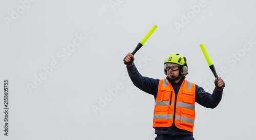 Airport ground crew officer in hi-vis vest signals direction with bright yellow paddles