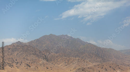 Mountainous region features rocky terrain and sparse vegetation beneath a clear blue sky, highlighting the natural landscape and geological formations
