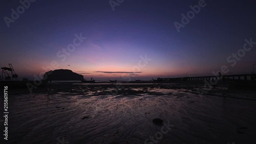 Twilight over tropical white sand beach with tidal flats, pier and palm trees