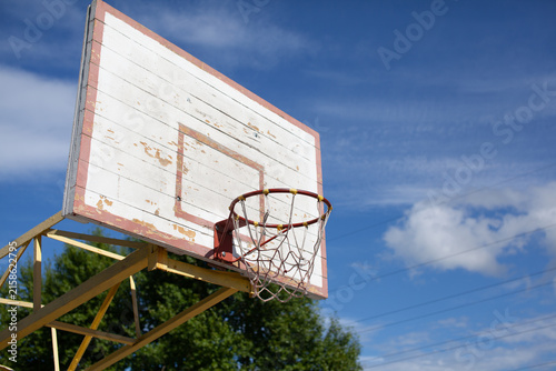 Quadro su tela Weathered basketball hoop with a damaged backboard set against a blue sky and sc