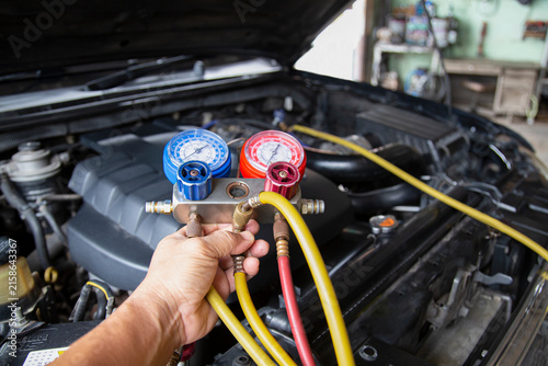 Bild auf Leinwand Mechanic hand holding manifold gauge set to check car air conditioning pressure in engine bay