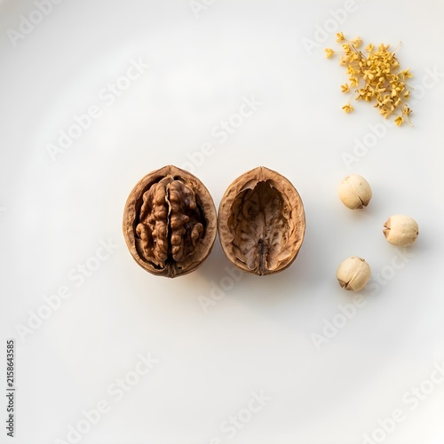 Top view flat lay of an open cracked walnut shell, dried lotus seeds, and yellow osmanthus flowers arranged cleanly on seamless white background.