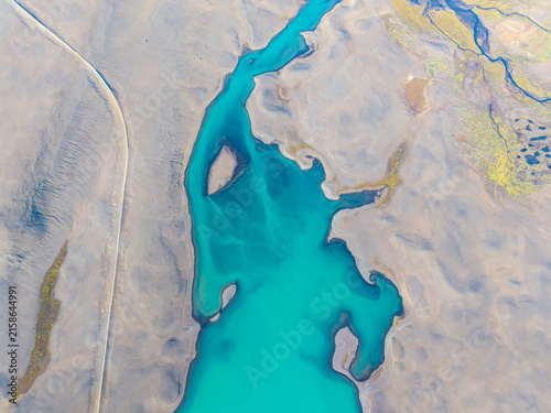 Aerial view of a vibrant turquoise glacial river winding through the barren, volcanic landscape of Iceland.