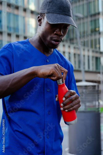 Fotografía Young black man opening red reusable water bottle, staying hydrated and healthy