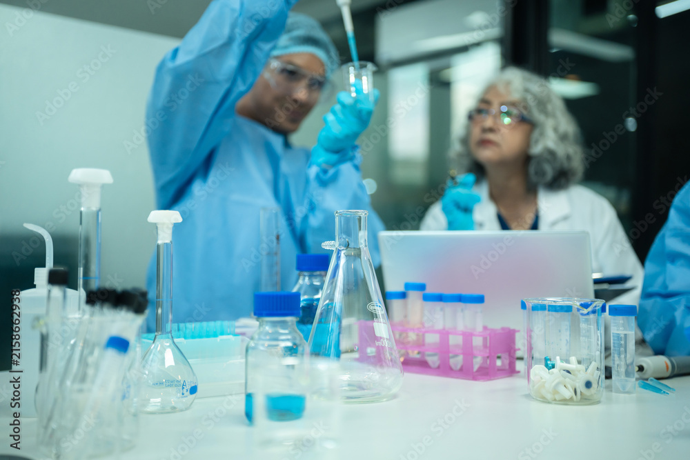 Fototapeta premium Team of medical laboratory technicians studying biotechnology sample with micro-scope and laptop for clinical trial.