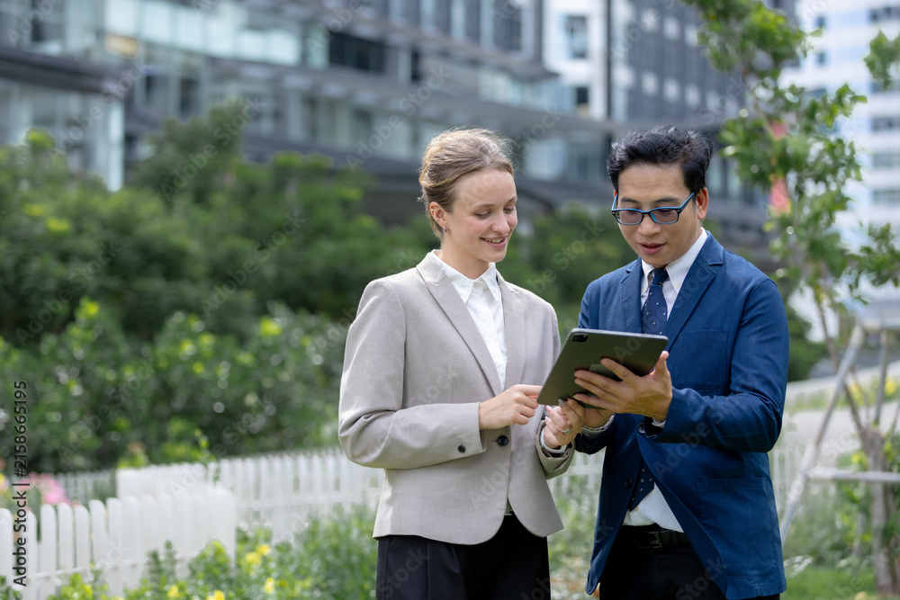 Fototapeta premium Business professionals reviewing tablet together outdoors, representing teamwork, collaboration, digital technology, communication, consulting, planning, partnership, corporate strategy.