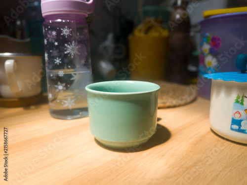 Картината върху платно Mint green ceramic mug on a wooden table in warm sunlight with blurred kitchenwa