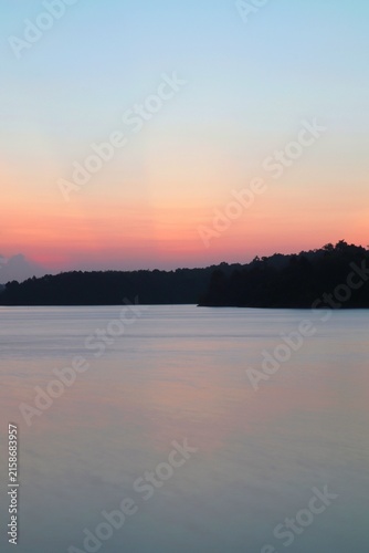 Foto Crepuscular rays and pastel twilight sky over calm lake water with tree line sil