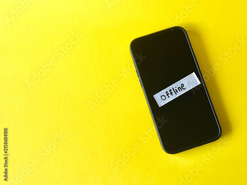 Flat lay of a smartphone on a yellow surface with a white strip of paper taped to the screen showing the handwritten word Offline.