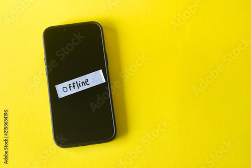 Canvas Print Flat lay of a smartphone on a yellow surface with a white strip of paper taped to the screen showing the handwritten word Offline