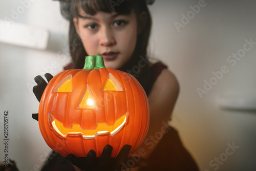 Girl is holding a Halloween pumpkin lantern towards the camera. selective focus