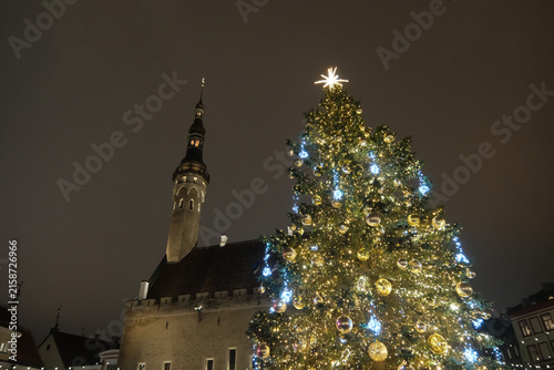 Low-angle view of an illuminated Christmas tree with Tallinn Town Hall tower in the background at night