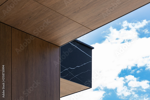 Konstfotografi Building corner overhang with black marble panel and wood cladding against cloud
