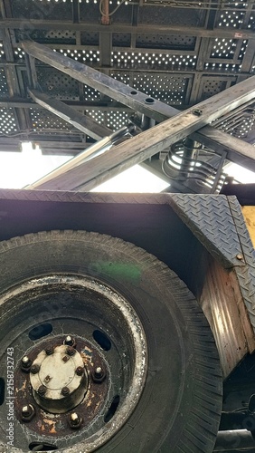 Close-up low-angle view of an old industrial vehicle showing a worn tire, hydraulic lifting mechanism, steel frame, and weathered metal components against the sky