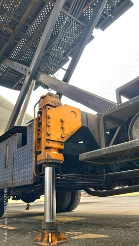 Close-up low-angle view of an old industrial vehicle showing a hydraulic lifting mechanism, steel frame, and weathered metal components against the sky