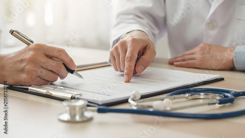 Close up of a doctor and patient reviewing medical documents and clinical records on a clipboard with a stethoscope lying on the desk office