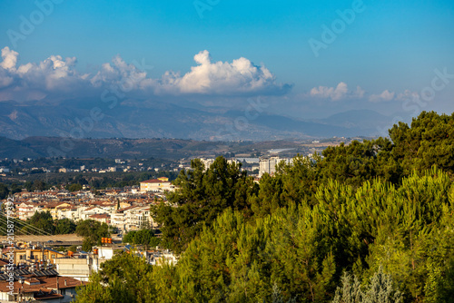Foto Scenic view from Turkbeleni hill on city of Manavgat, lush pine forest on foreground and majestic Taurus Mountains on background under blue sky with clouds