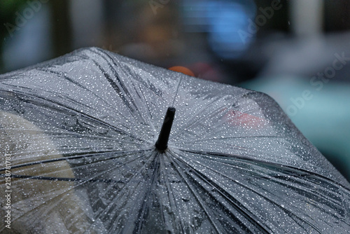 Curved canopy of a clear vinyl umbrella covered with droplets fills the frame against a blurry urban background in Japan.
