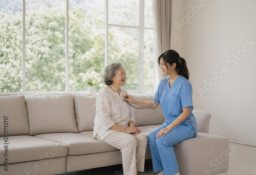 Nurse checking heartbeat of elderly woman with stethoscope at home