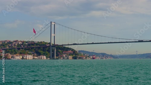 Panoramic view of the iconic Bosphorus Bridge connecting Europe and Asia with lush green hills and urban landscape under a cloudy sky in Istanbul