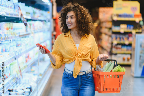 Woman grocery shopping using phone in supermarket aisle