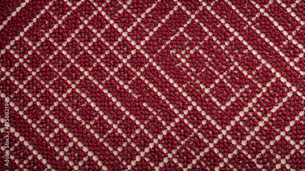 Fototapeta premium Red cross-stitch embroidery pattern on beige fabric background texture