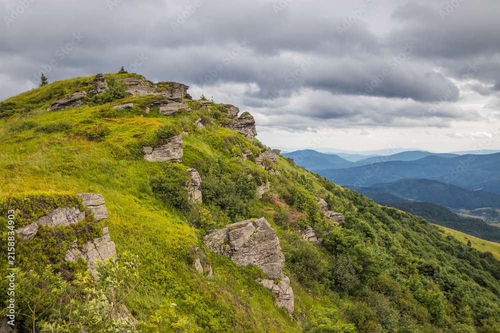 Naklejka premium Serene landscape of a grassy hill with grey rock outcrops under a moody and cloudy mountain sky